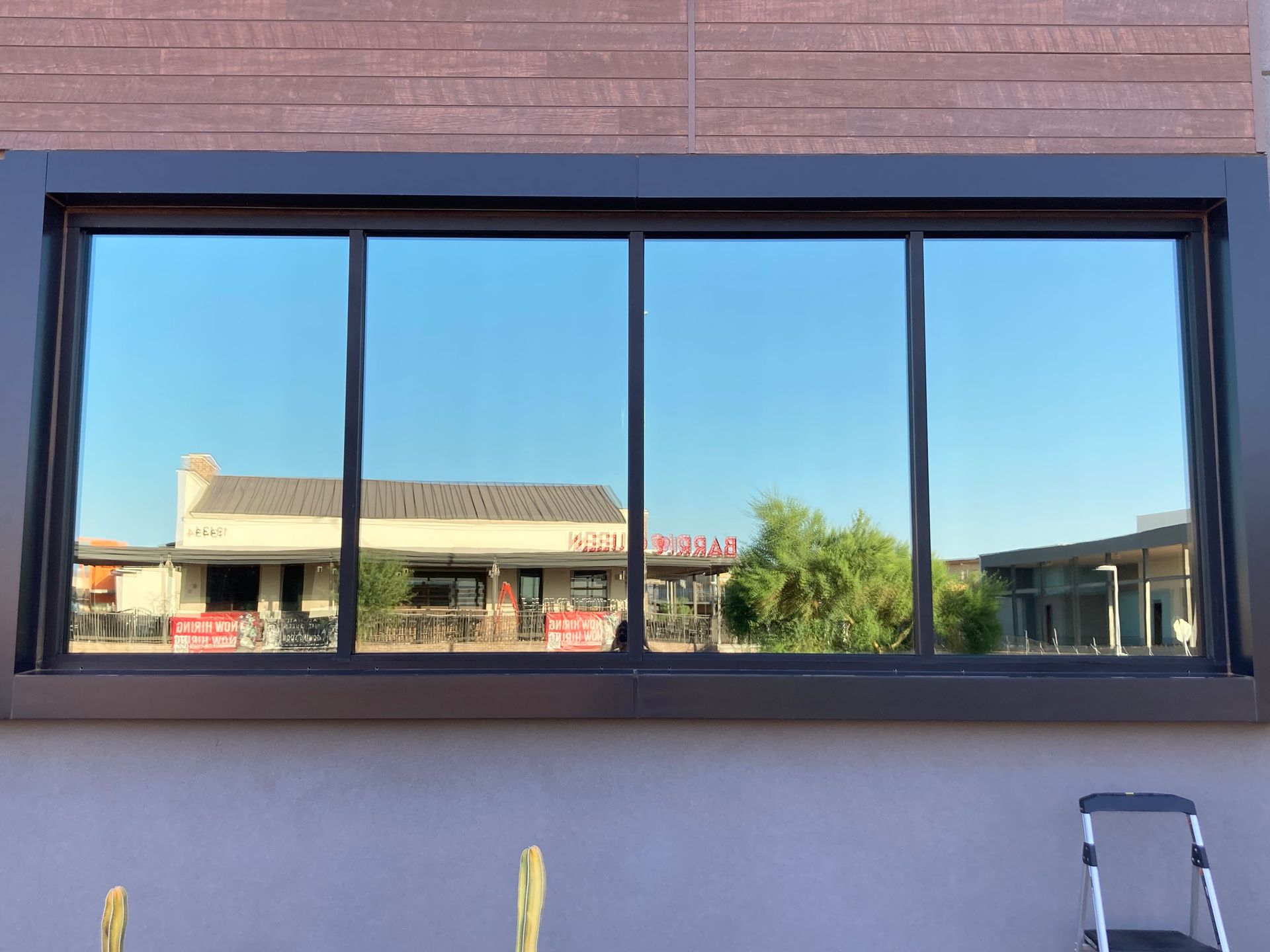 A large, rectangular window with a dark frame set into a light-colored wall, reflecting a suburban strip mall outside.