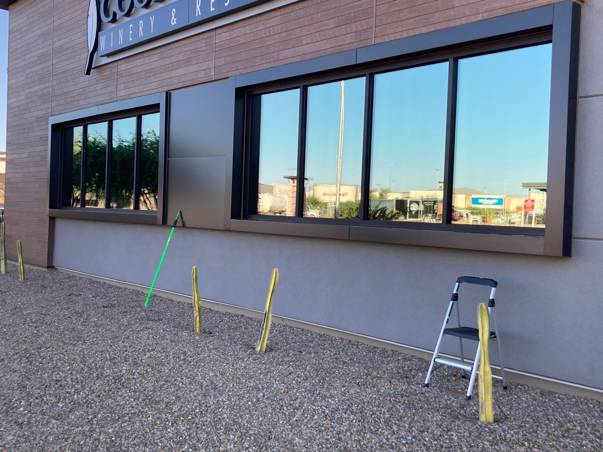 Exterior of a building with large reflective windows, gravel ground, and a small metal step ladder near the wall.