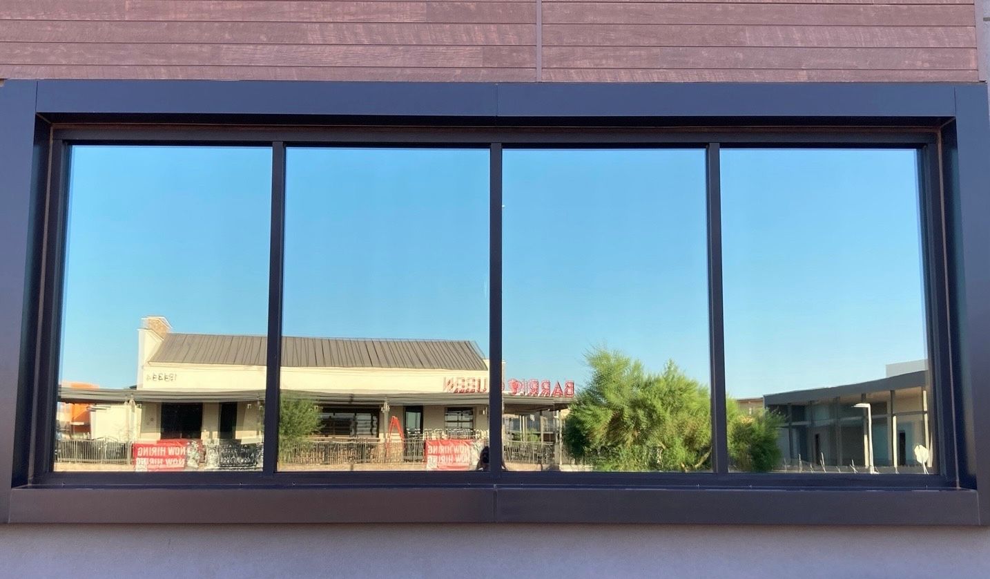 Large rectangular window with a dark frame, reflecting a nearby building and trees under a clear blue sky.