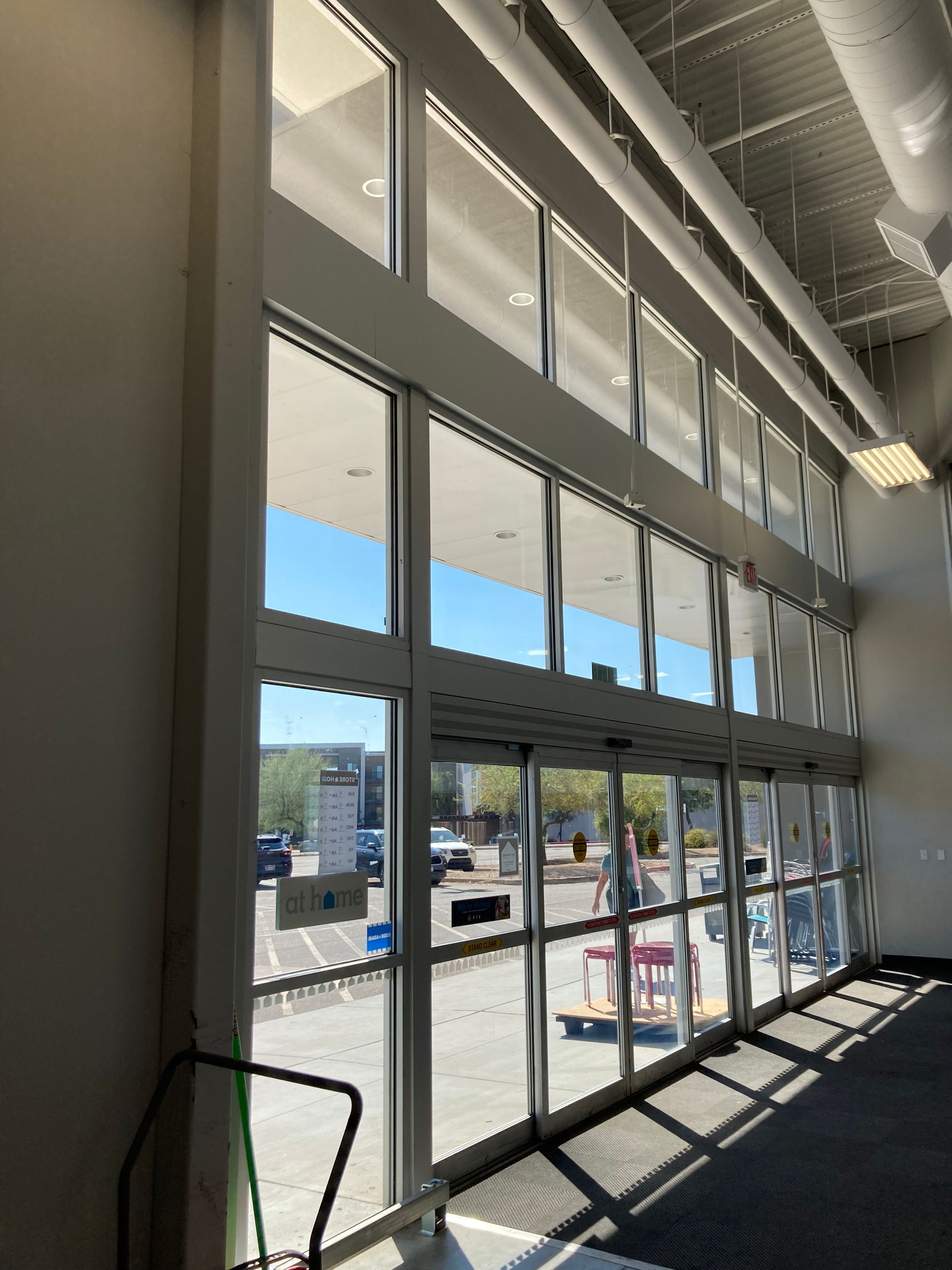 View from inside a large commercial building looking out through tall glass sliding doors to a parking lot under a canopy.