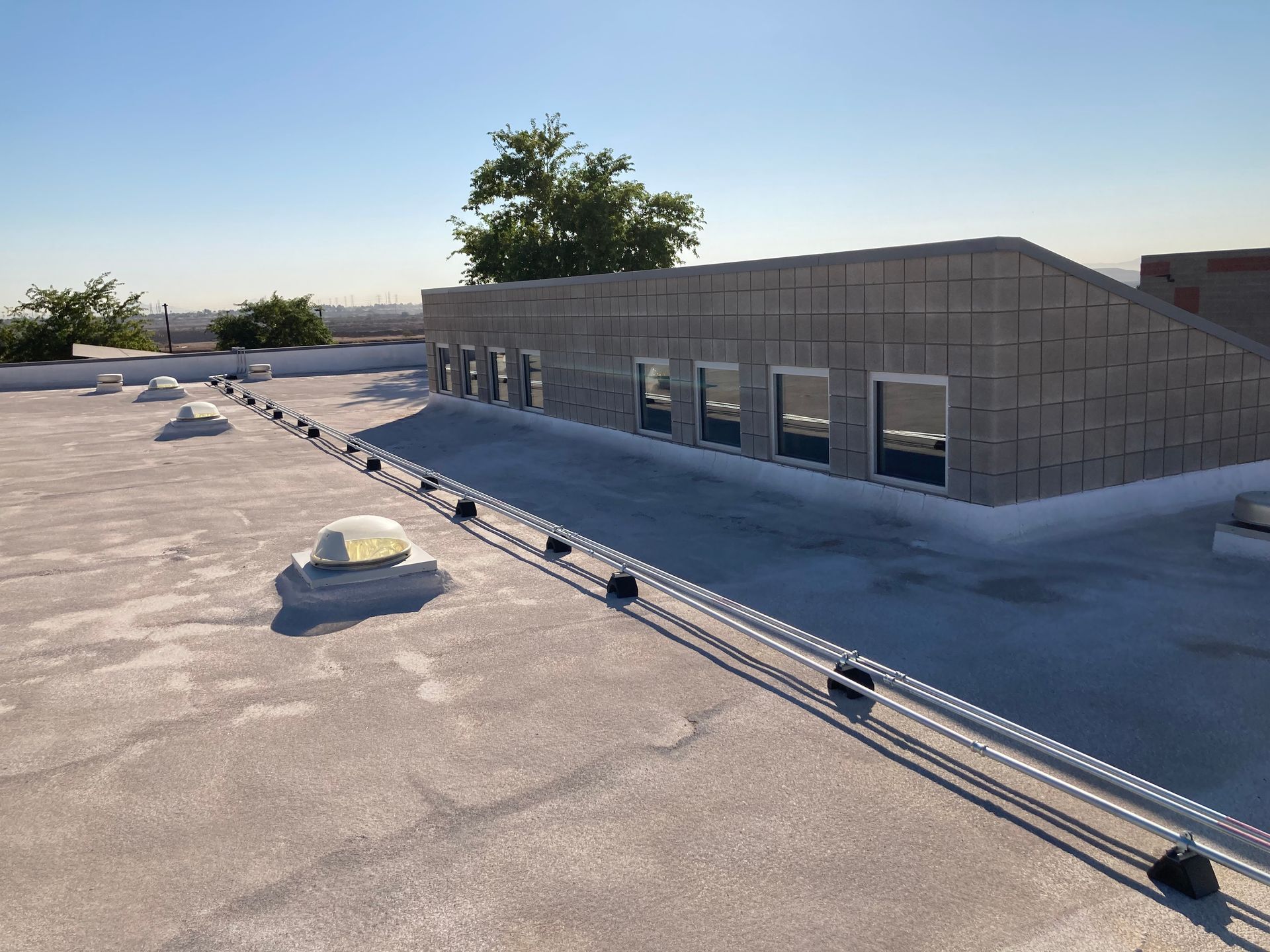 A low-angle view of a grey concrete rooftop structure with multiple windows, featuring a safety railing and skylights.