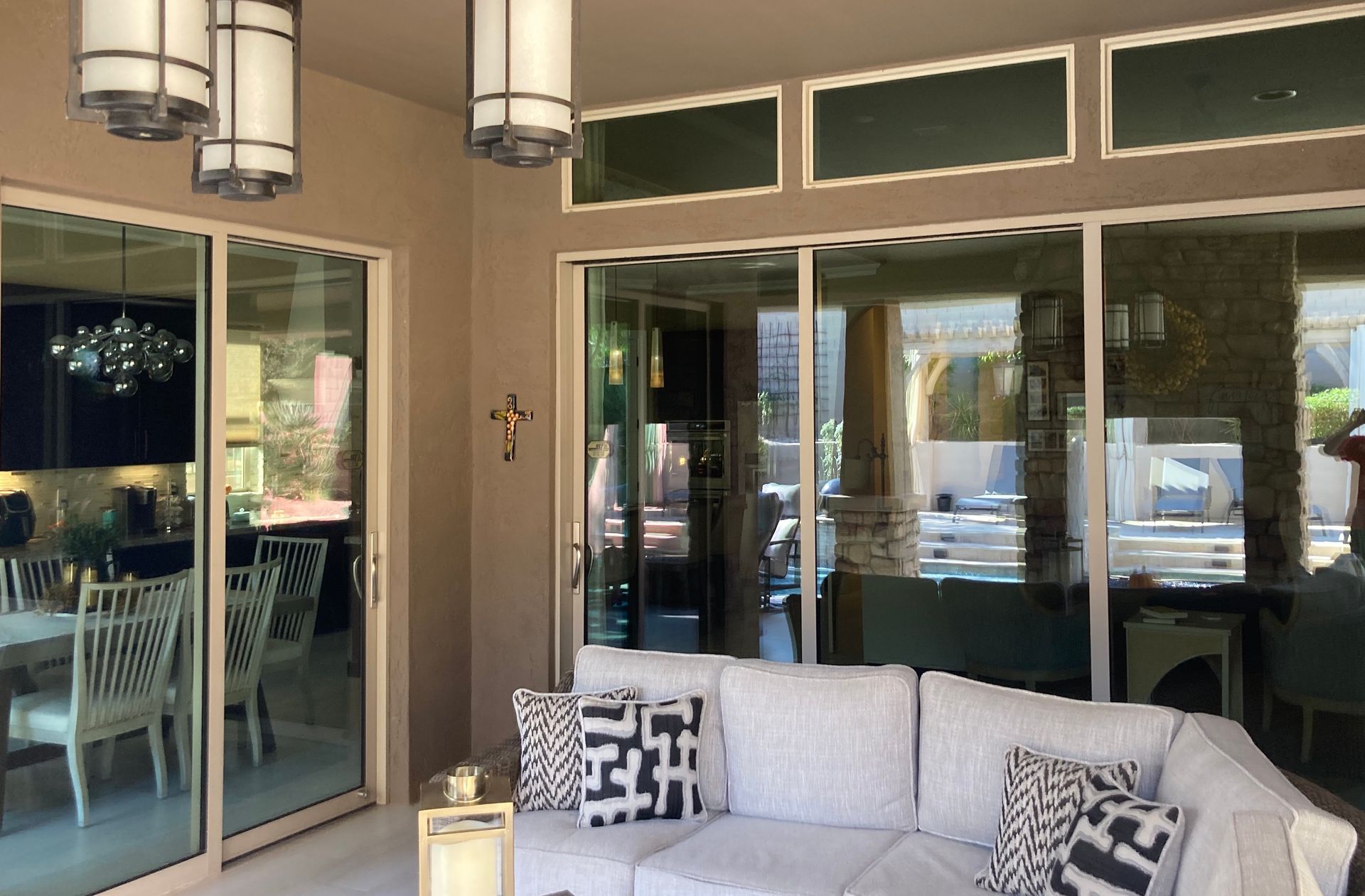 A bright, modern patio with a white sectional sofa, patterned throw pillows, and sliding glass doors revealing a dining room.