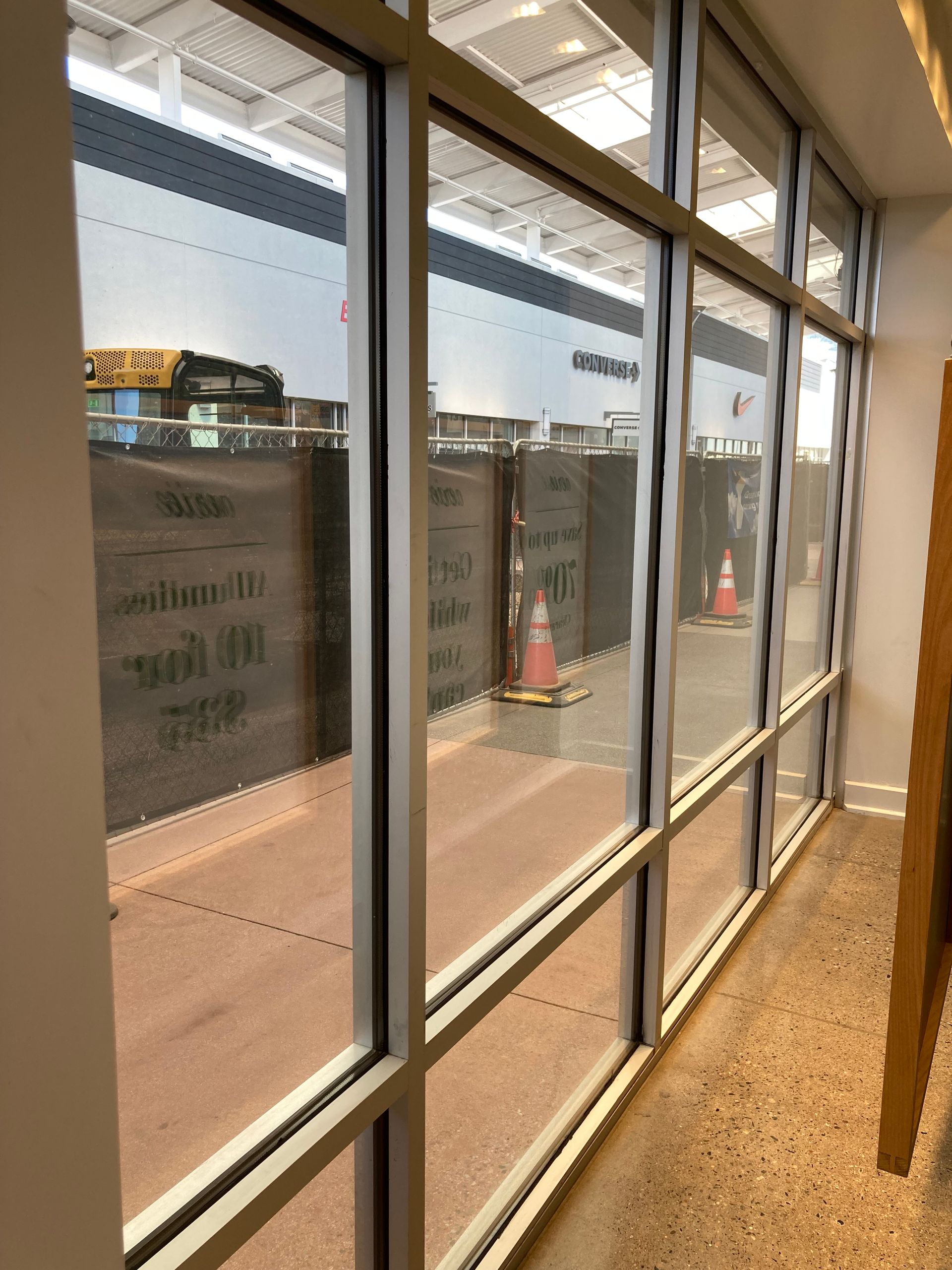 A view through large glass windows of a bus at a construction site with orange safety cones on a concrete path.
