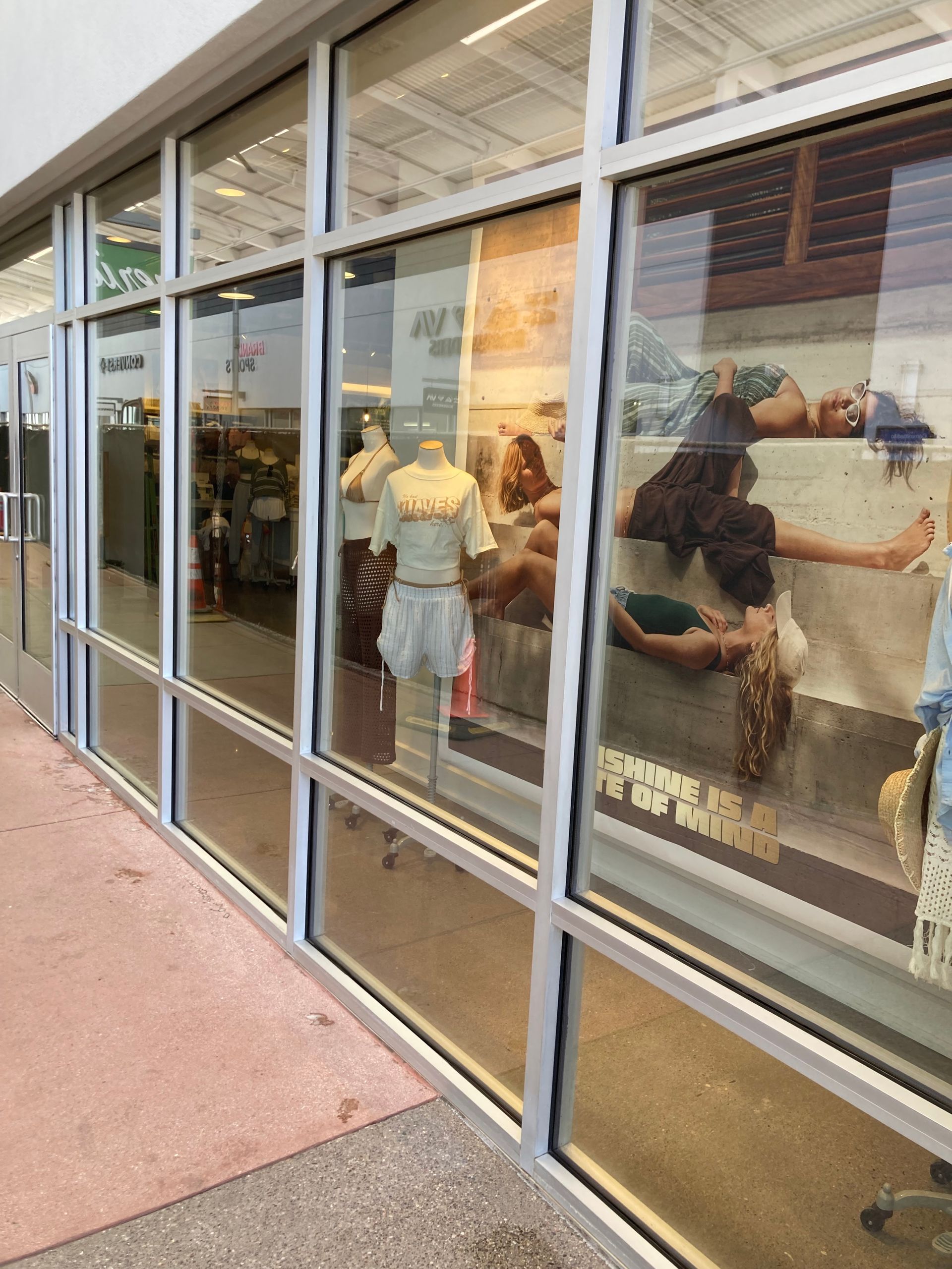 Storefront display featuring clothing on mannequins and large window decals of people lounging on a sandy beach.