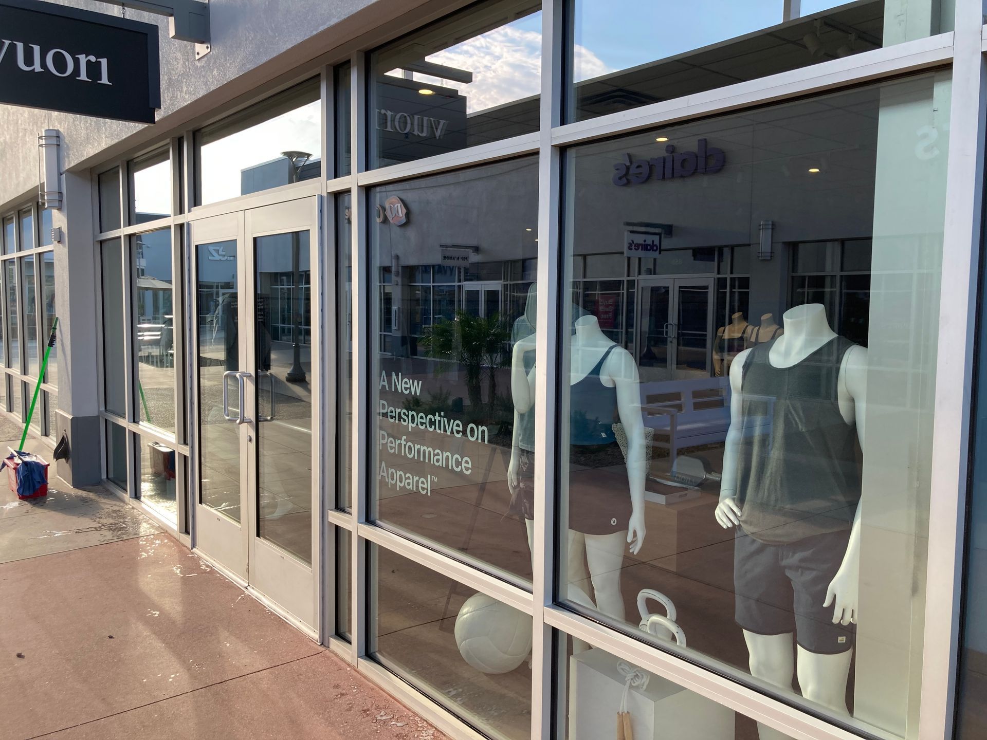 Storefront of a Vuori clothing shop featuring window displays with mannequins in athletic wear on a sunny day.
