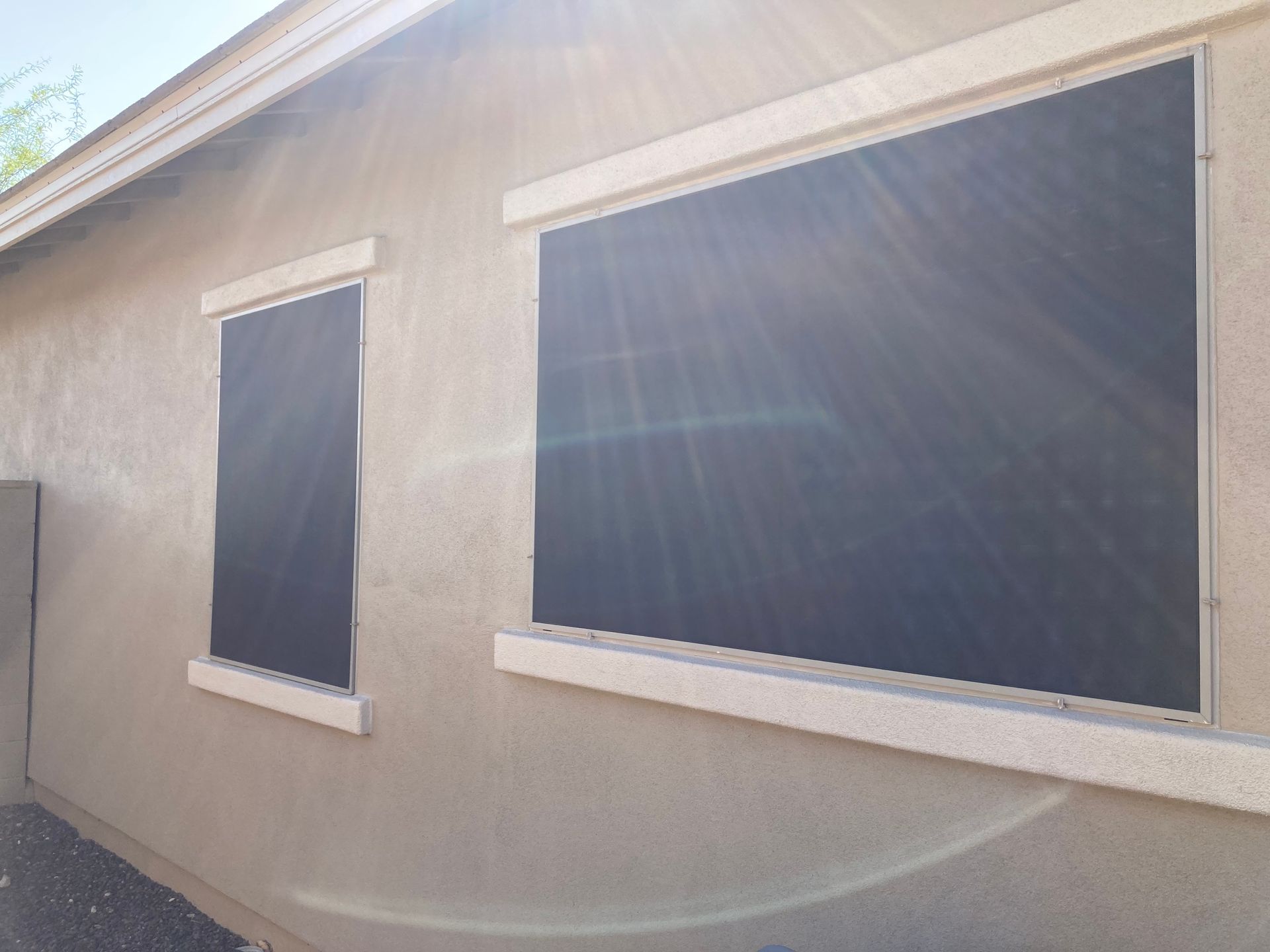 Two rectangular windows on a tan stucco wall, both covered by dark, tightly-fitted exterior solar shade screens.