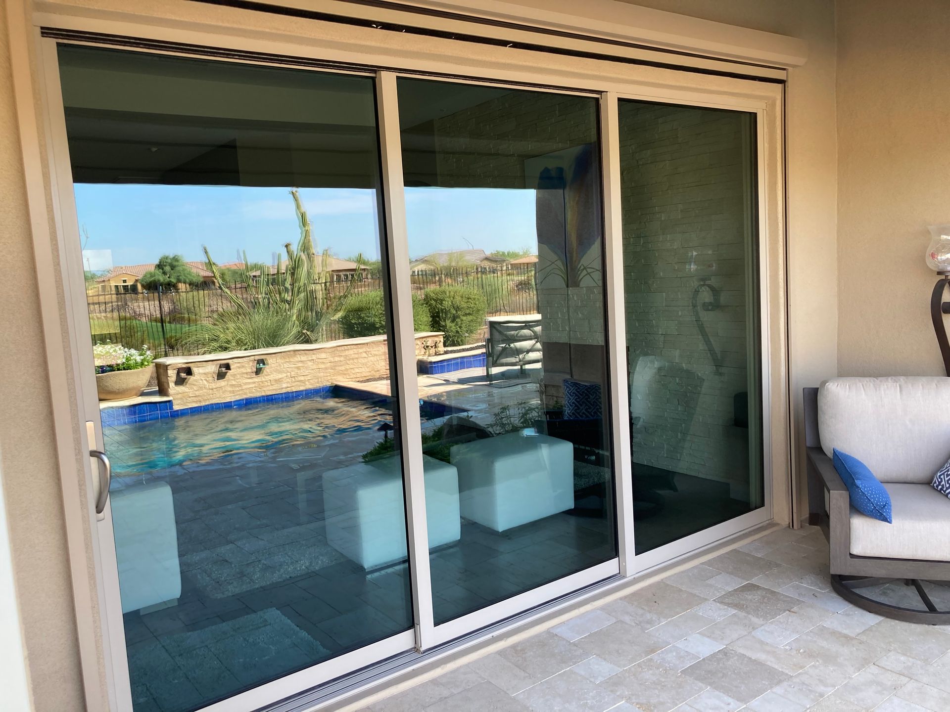 A sliding glass patio door reflects a backyard pool and landscape, with a beige outdoor chair to the right.