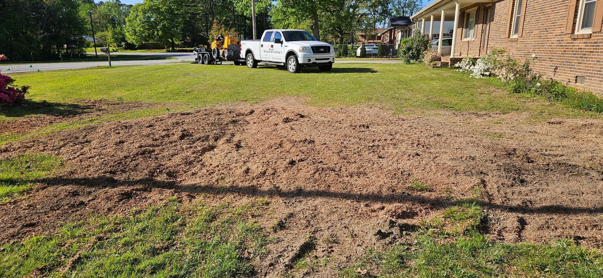 A yard with tilled soil in the foreground, a truck, and a house in the background.