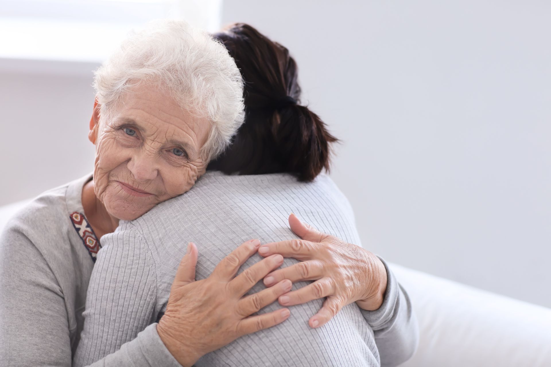 Une femme âgée serre dans ses bras une femme plus jeune sur un canapé.