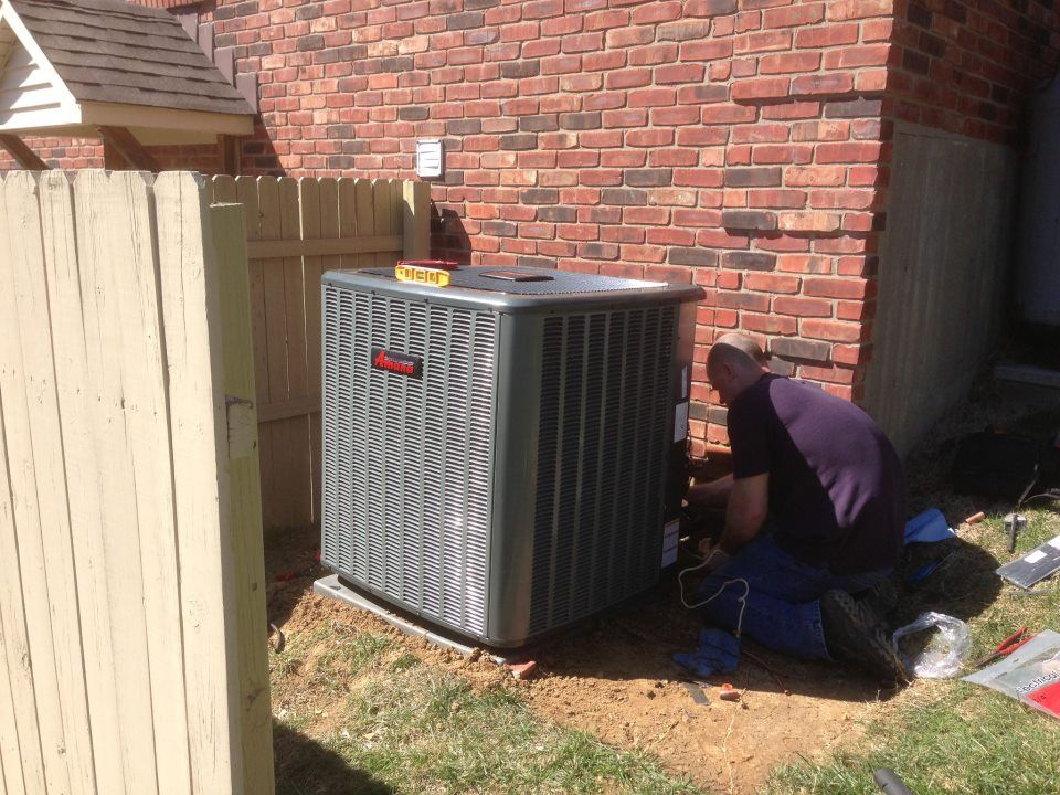 A man is working on an air conditioner outside of a brick house.