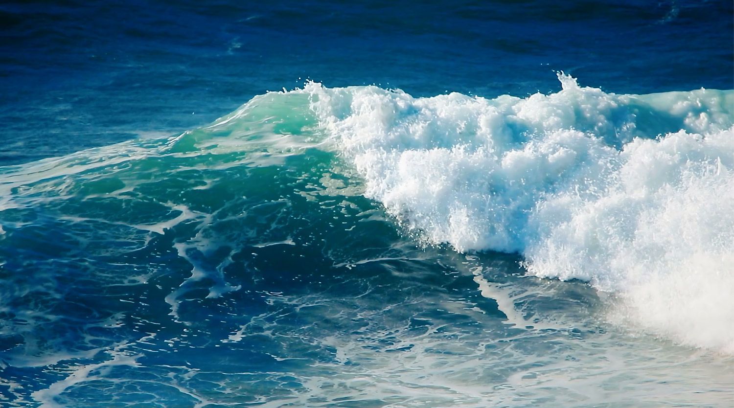 Meereswellen brechen sich, türkisfarbenes Wasser und weißer Schaum.