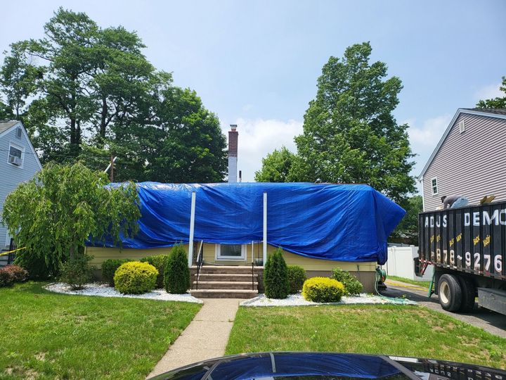 A house is covered in a blue tarp and a dumpster is parked in front of it.