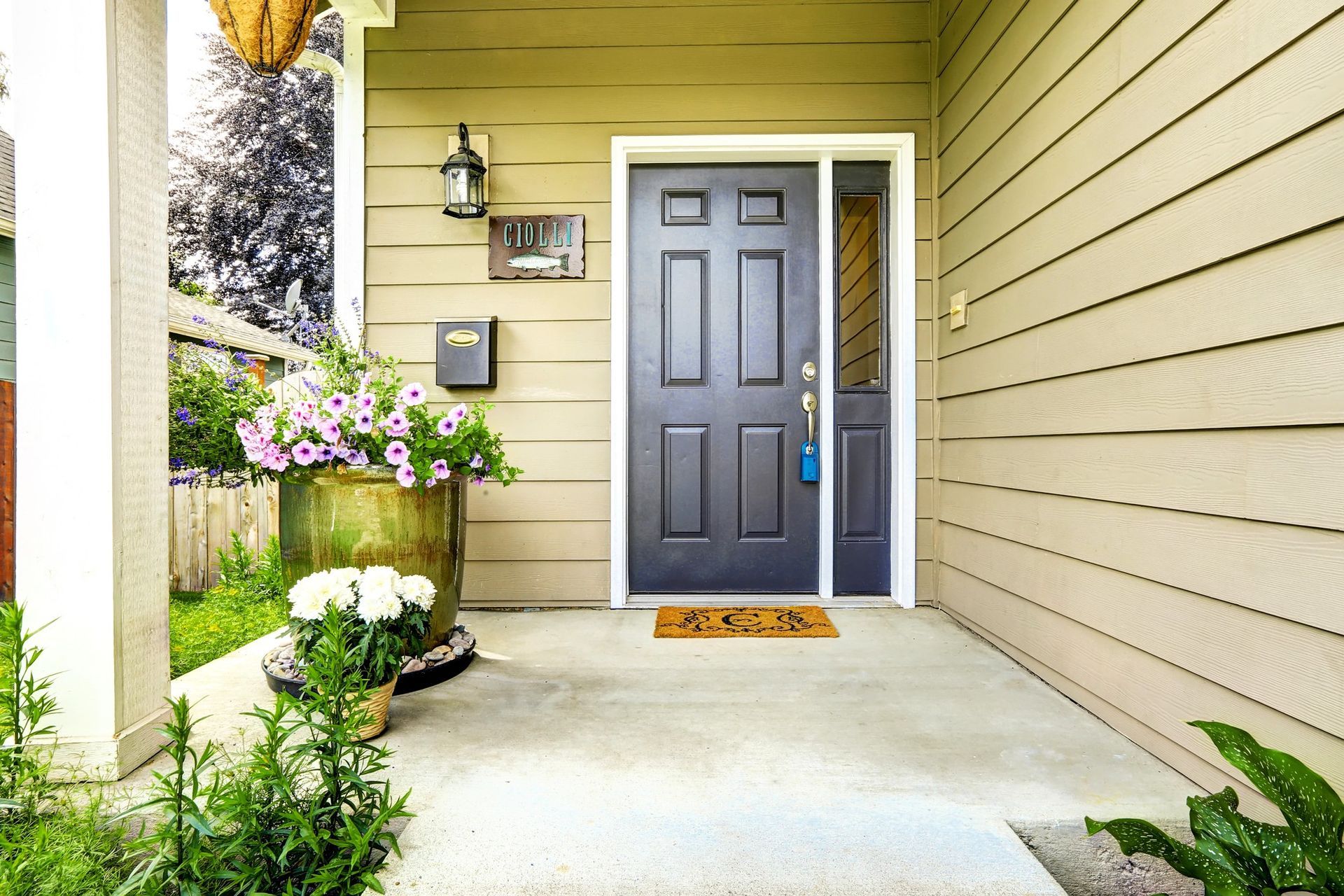 Concrete porch with dark door, flower pots, doormat, and greenery