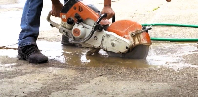 A man using a circular saw to cut and remove concrete.
