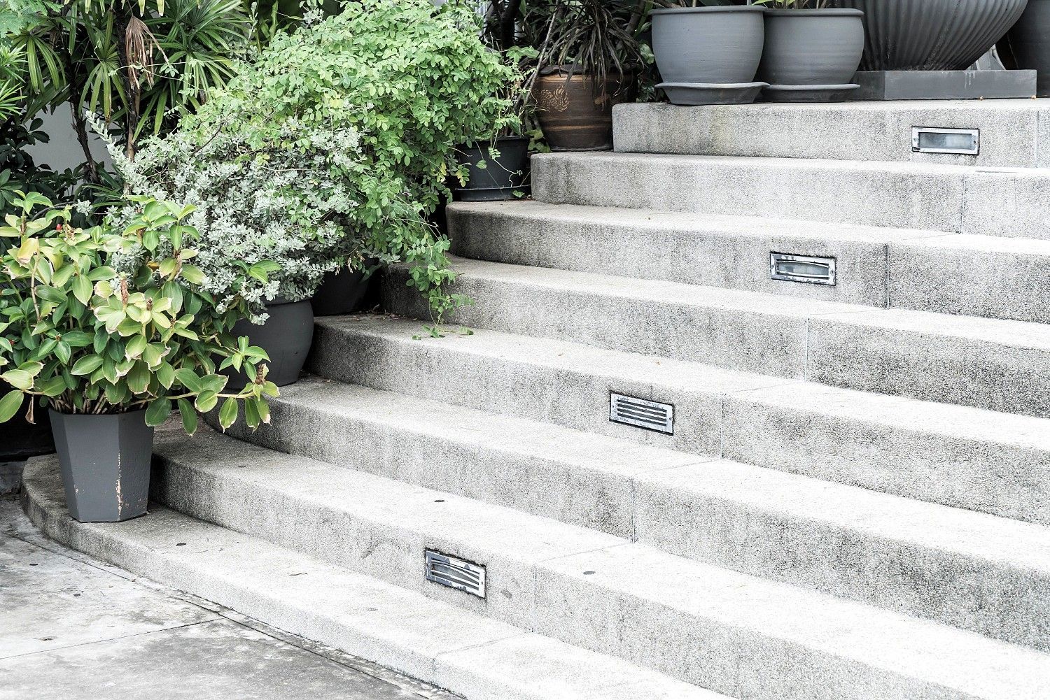 Gray concrete steps with potted plants and metallic vents set into the surface