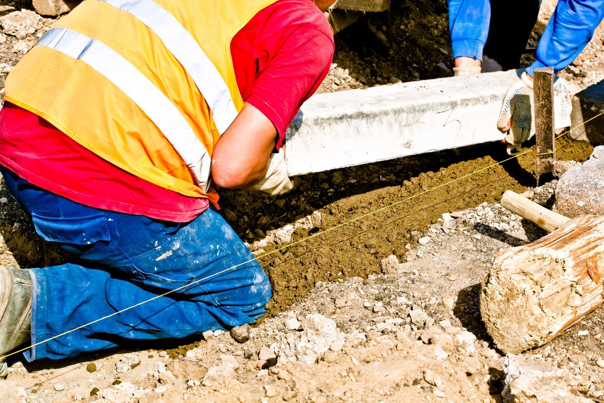 Construction workers in high-visibility jackets installing a concrete curb on a residential street.