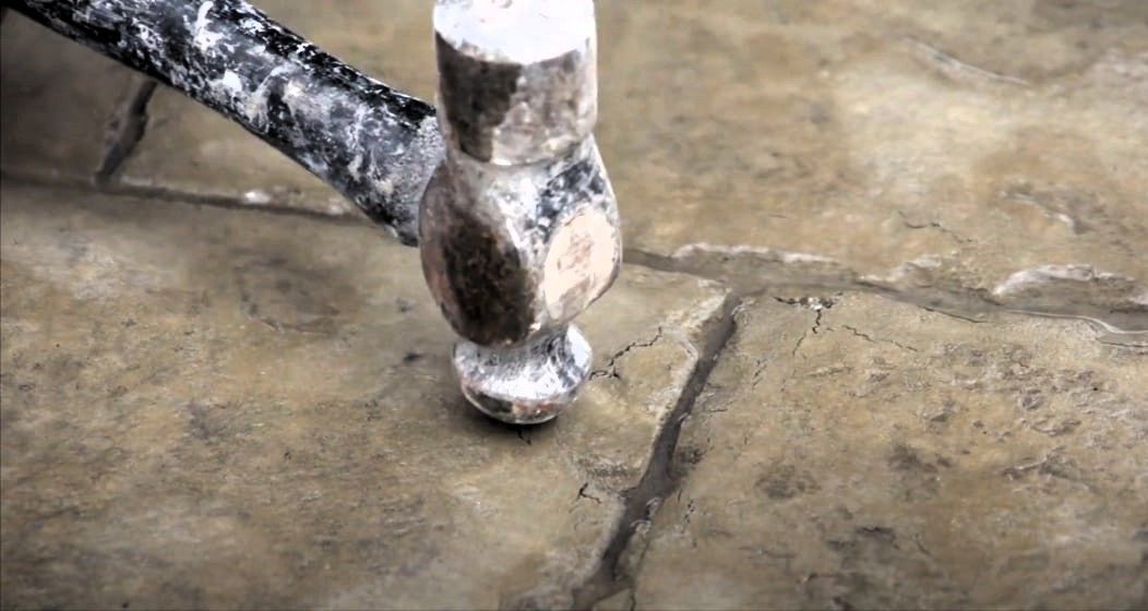 Stamped concrete crack being pointed out with a hammer