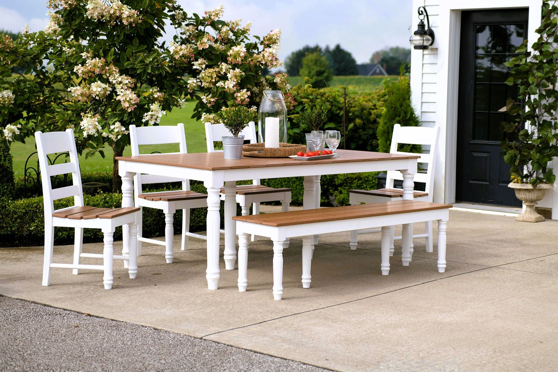 Concrete patio dining area with a white and wooden table set, flowers, and a refreshment tray.
