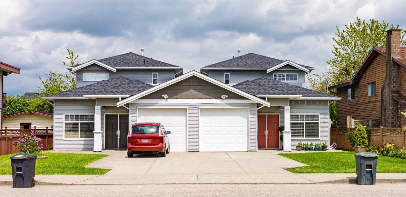 A home with a red car parked outside the garage over a pristine concrete driveway