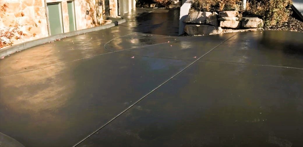 Concrete driveway with stone wall and garage doors in sunlight.