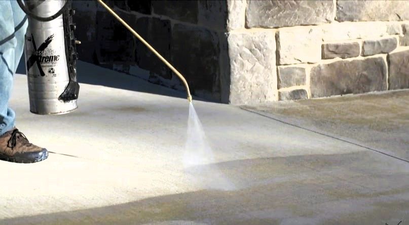 Pressure washing and sealing a concrete floor with a stone wall behind it.