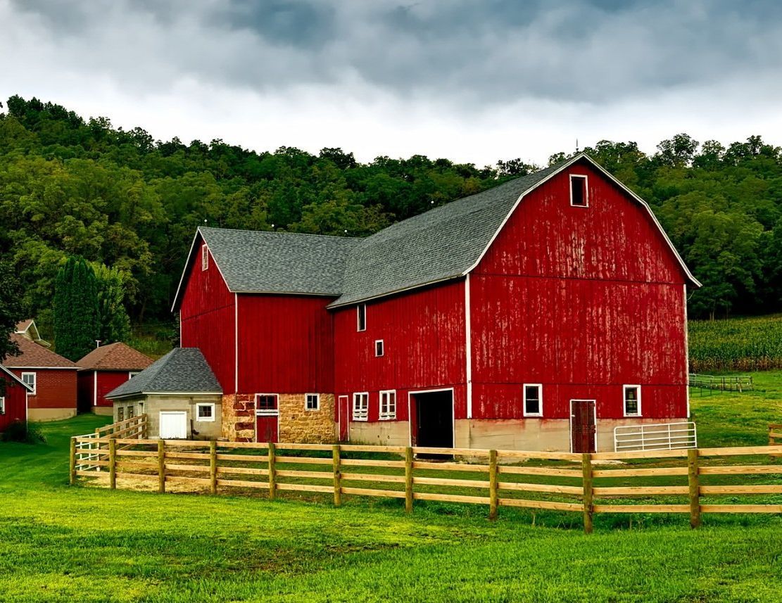 A red barn is surrounded by a wooden fence in a grassy field.