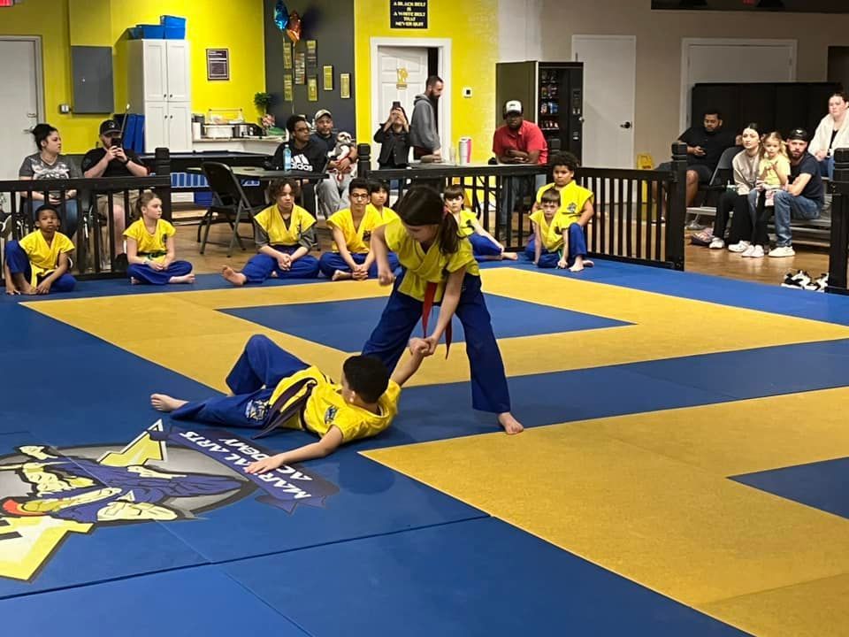 A group of children are practicing martial arts on a blue and yellow mat.