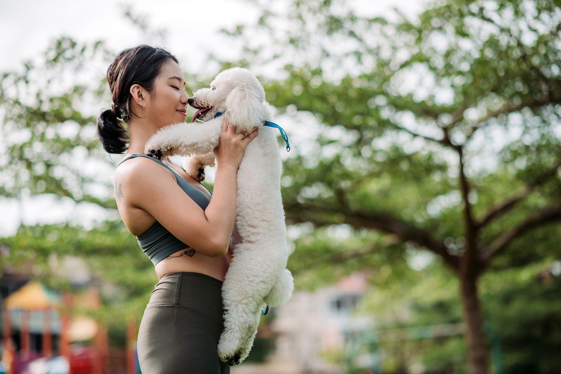 Woman holding a white poodle, nose to nose, in a park.