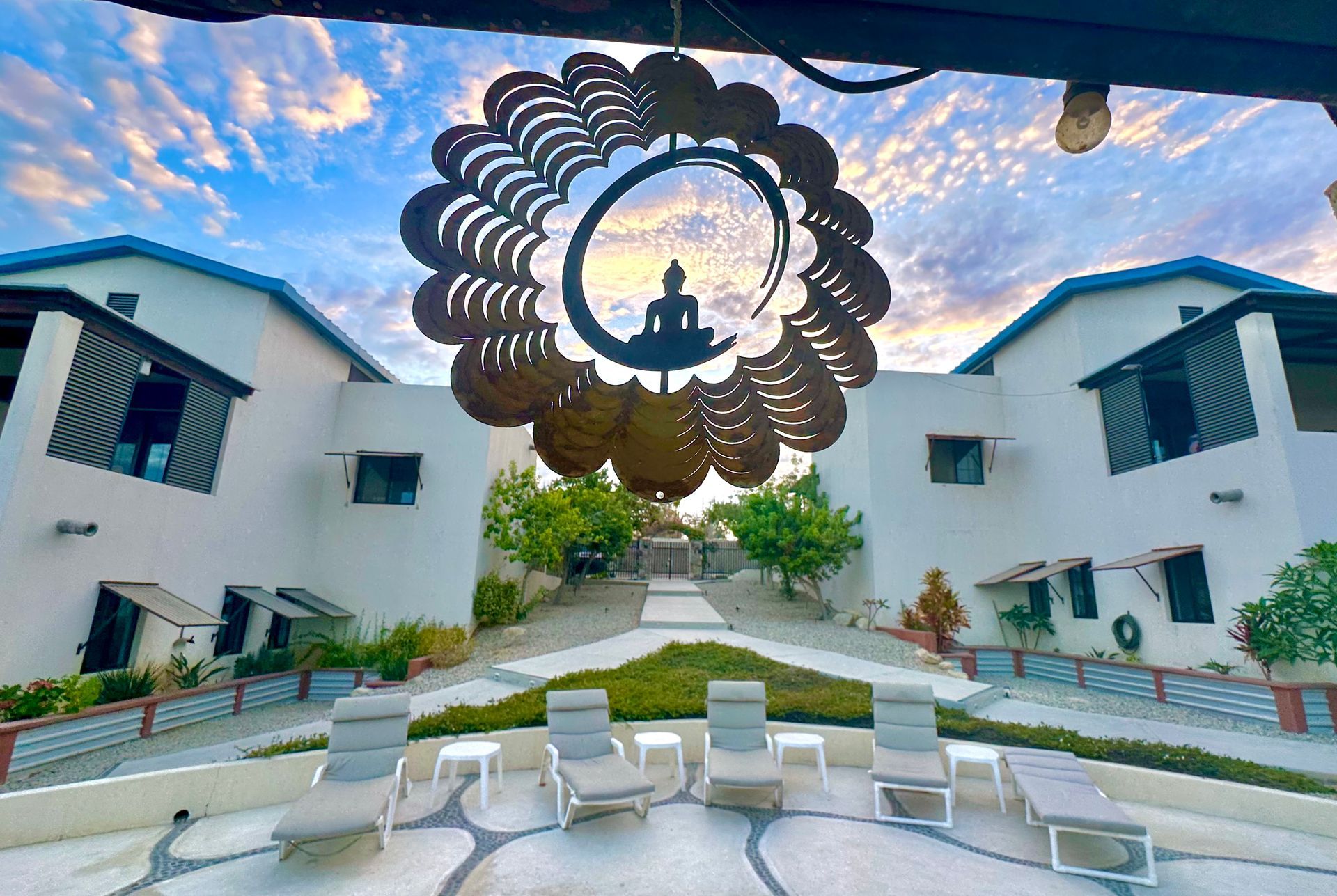 Exterior view of white buildings with a decorative Buddha sculpture against a sunset sky; lounge chairs in foreground.