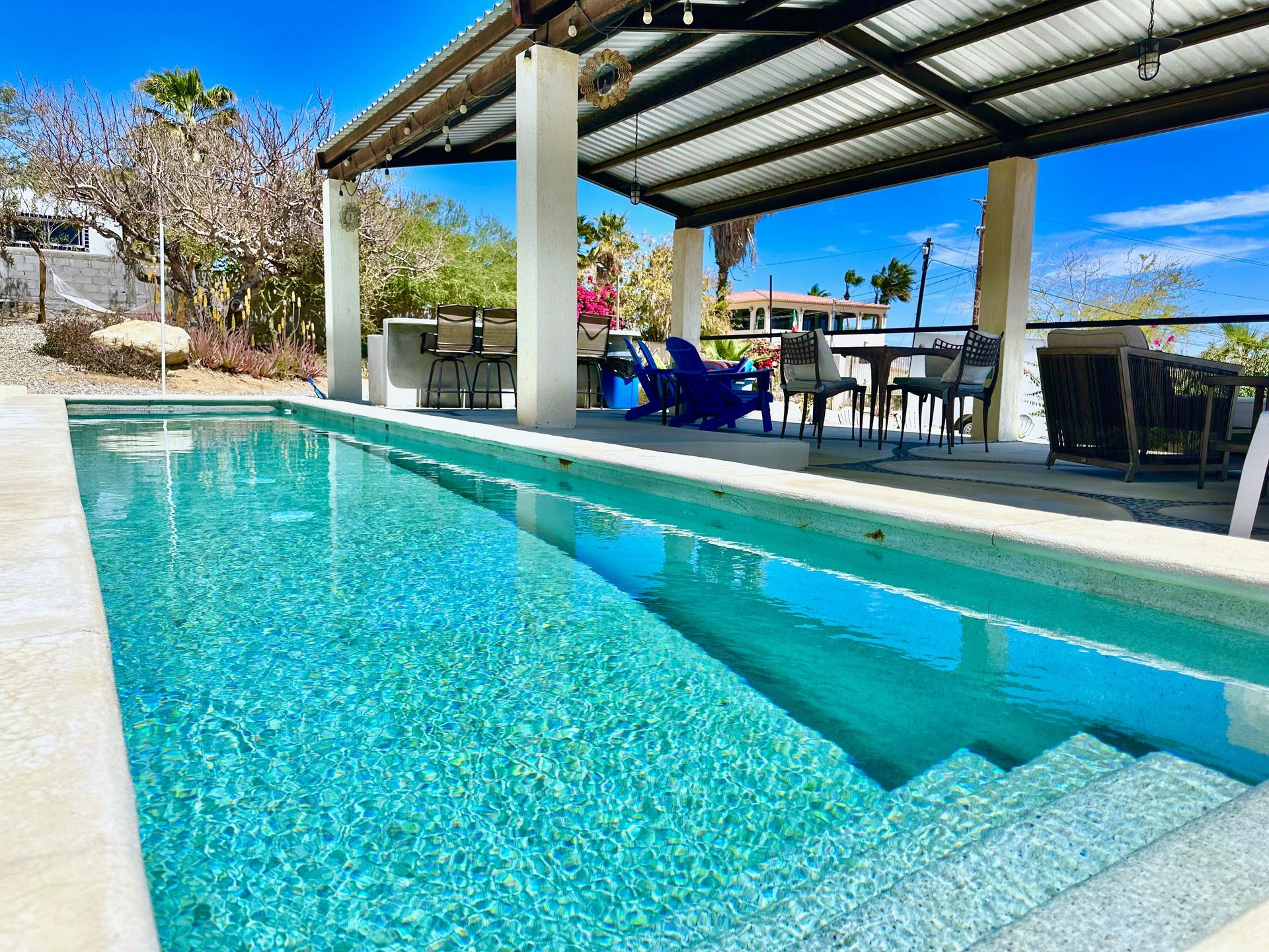 Swimming pool with covered patio, outdoor seating, and clear blue water.
