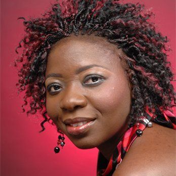 A woman with curly hair and earrings is smiling for the camera.