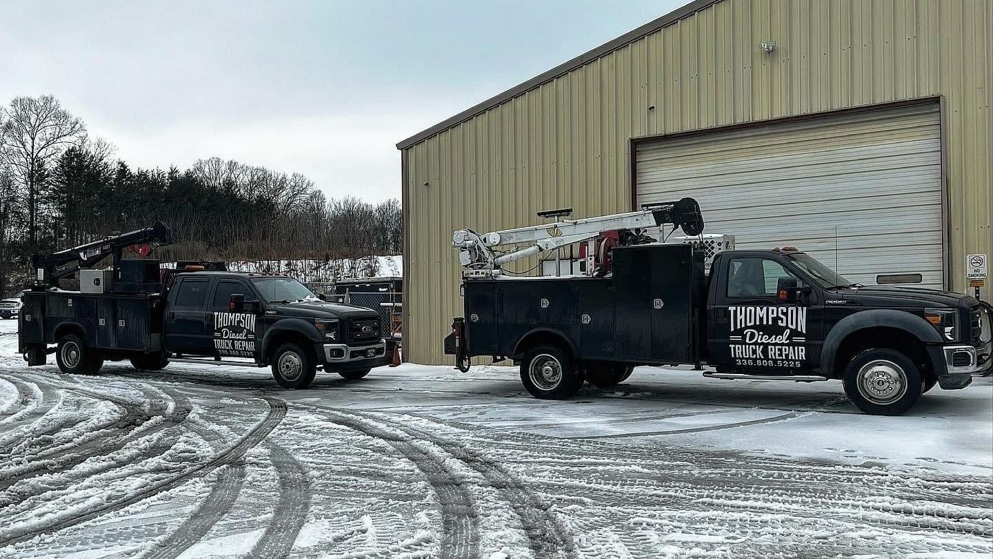 Two trucks are parked in the snow in front of a building.