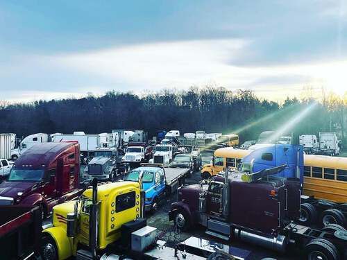 A lot of trucks and buses are parked in a lot.