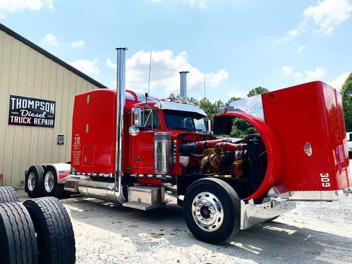 A red semi truck with its hood open is parked in front of a building.