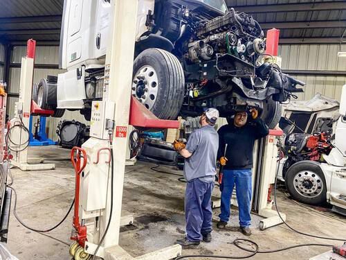 Two men are working on a semi truck in a garage.