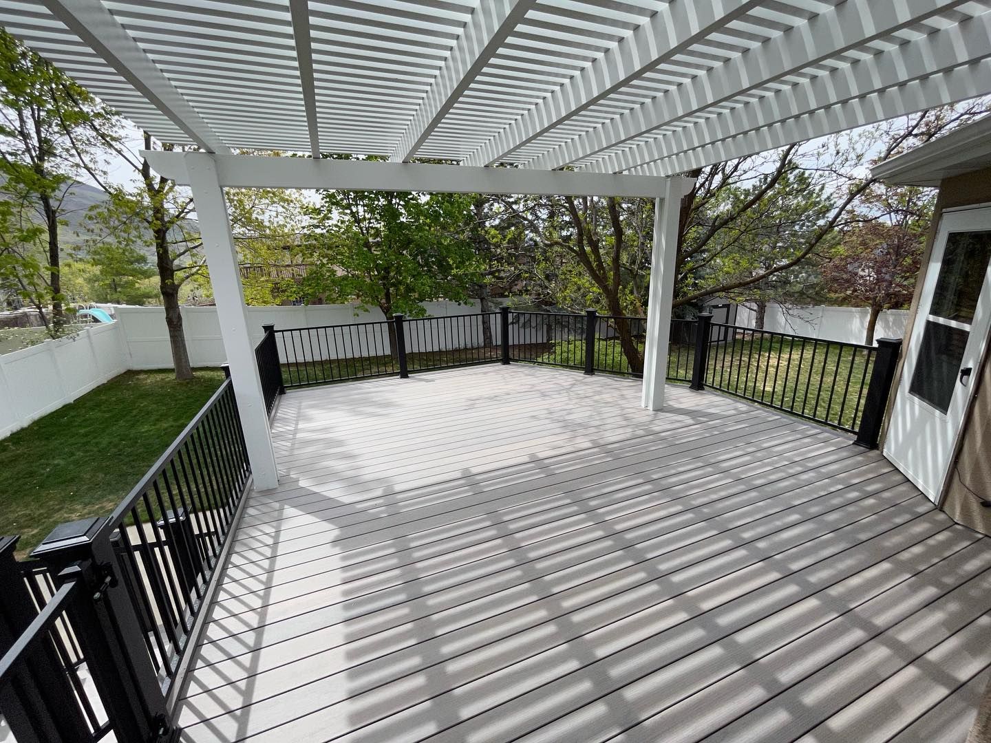 A large patio with a white pergola and a black railing.