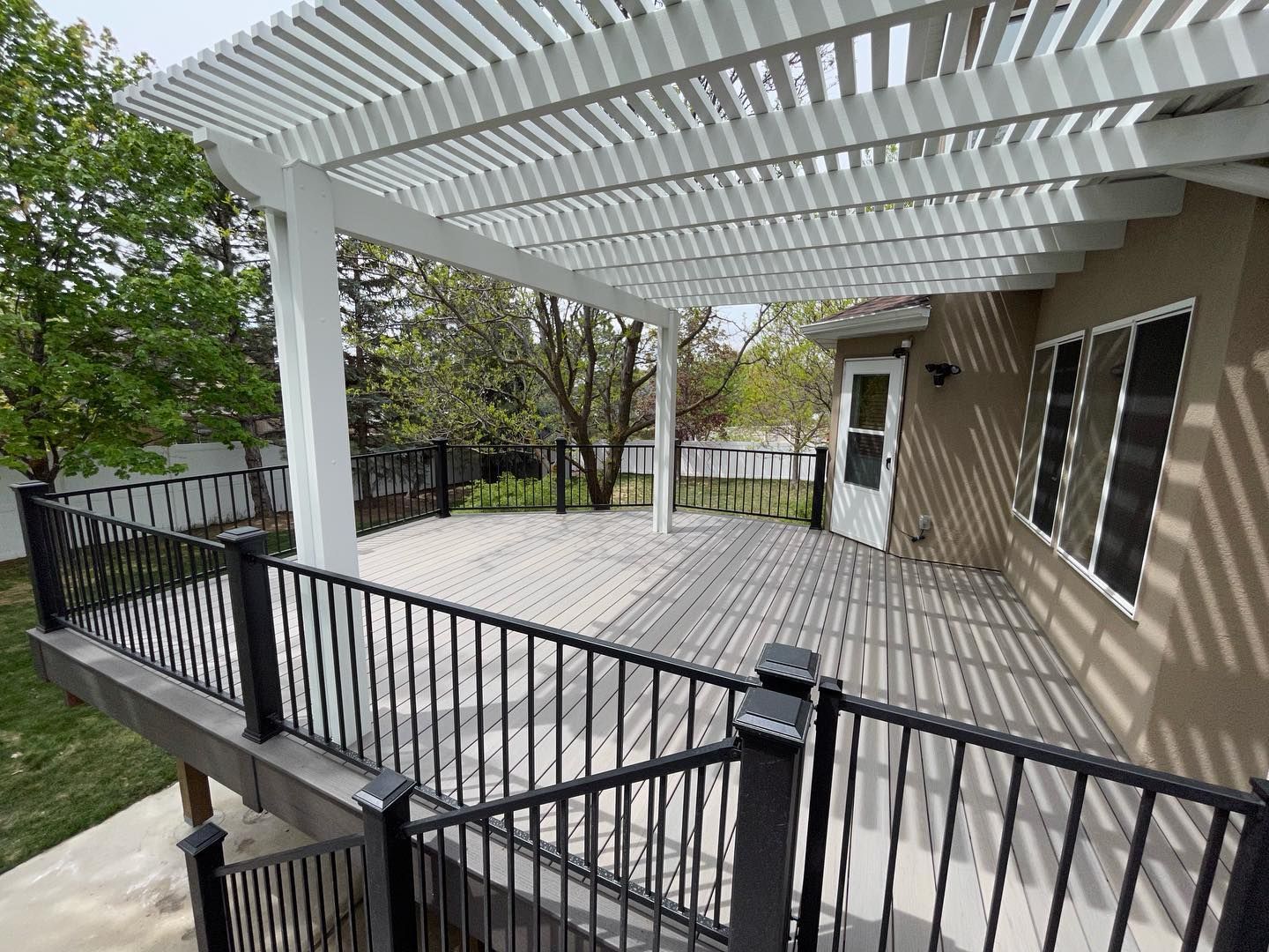 A large deck with a white pergola and a black railing.