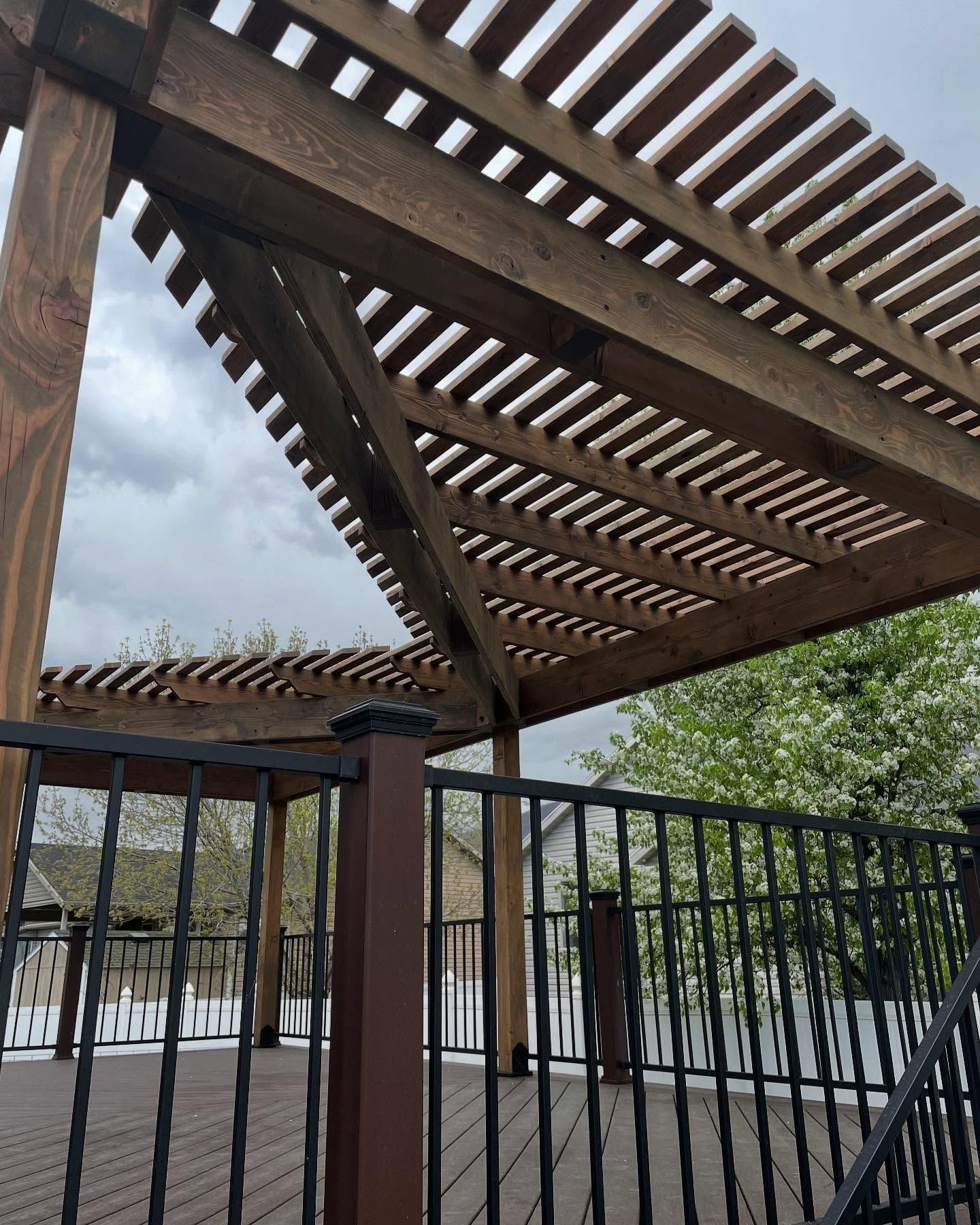 A wooden pergola with a metal railing on a deck.