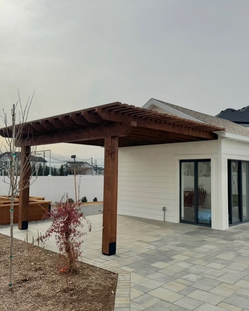 A white house with a wooden pergola in front of it.