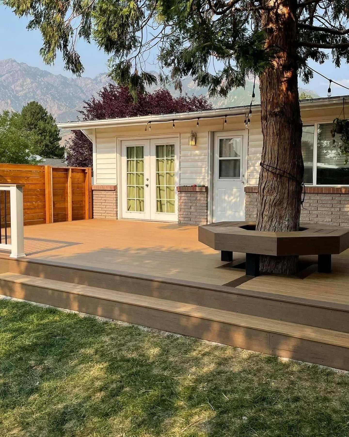 A house with a large deck and a tree in front of it.