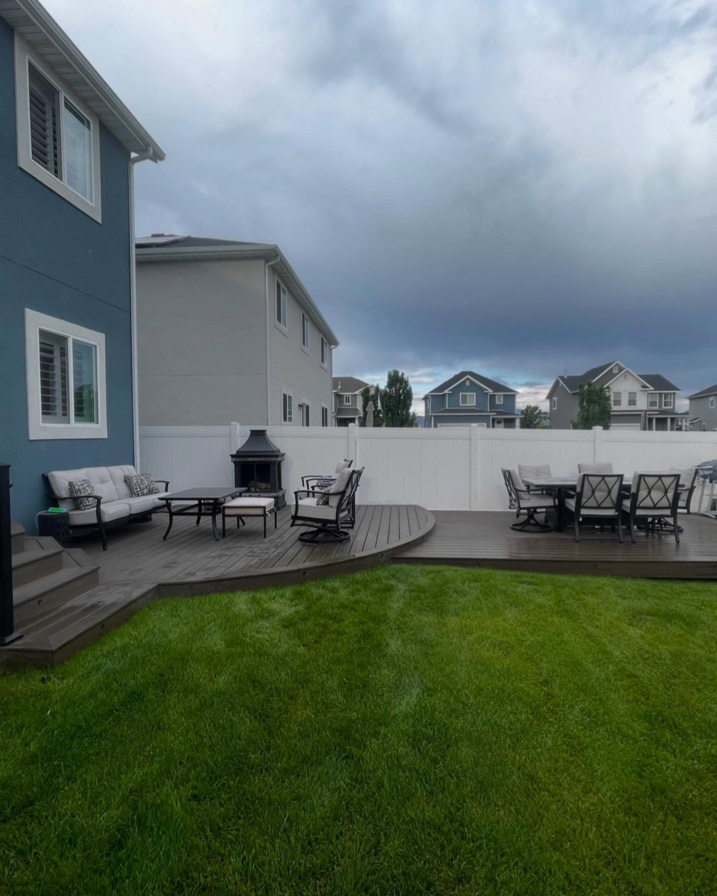A backyard with a wooden deck , patio furniture , and a white fence.