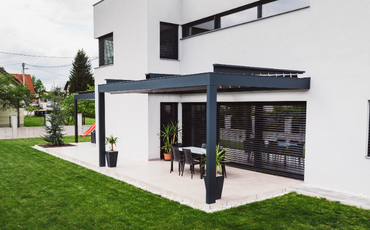 modern backyard with a concrete patio, a black awning, black flower pots, and black patio furniture.