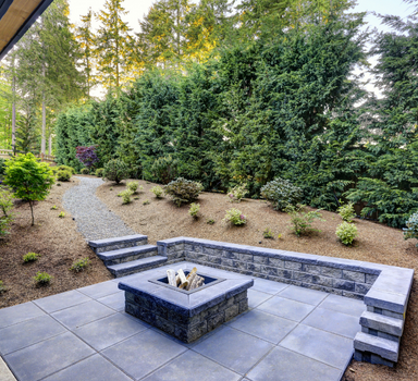 concrete patio slab with a fireplace in the center and steps leading down to it from the forest