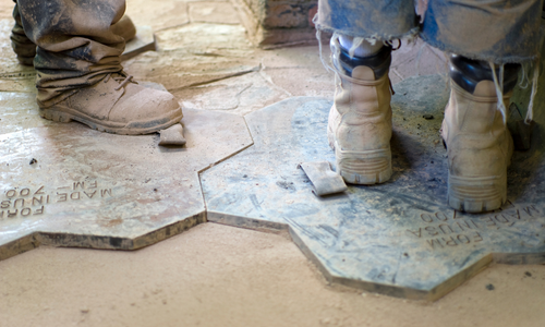 Workers boots standing on top of stamp tool that is used for stamped concrete designs