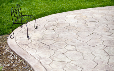 Patio made of stamped concrete that has a black wire patio chair sitting in the top left corner.