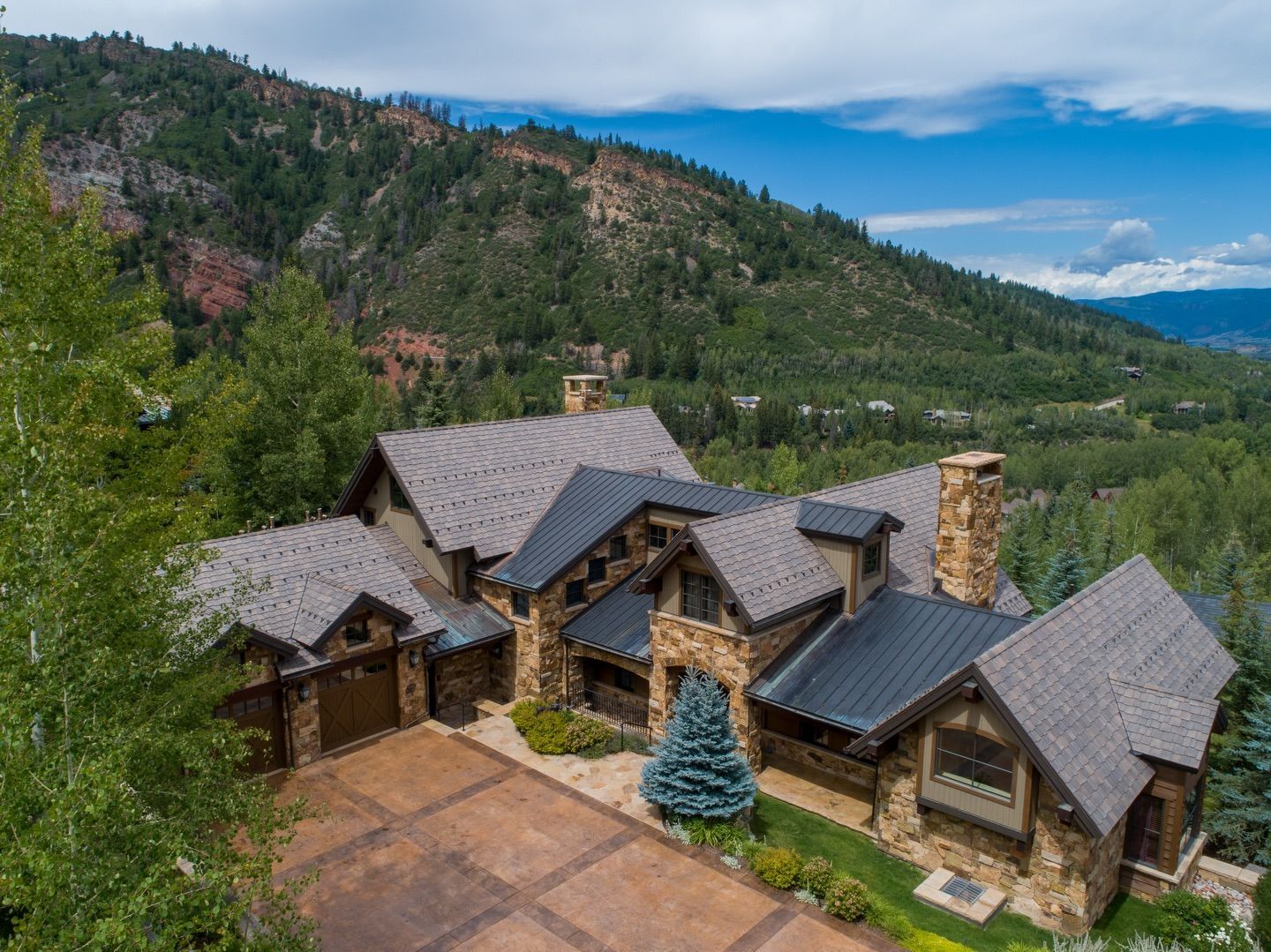 Stone mountain home with gray roof and stone chimney in a forested hillside setting