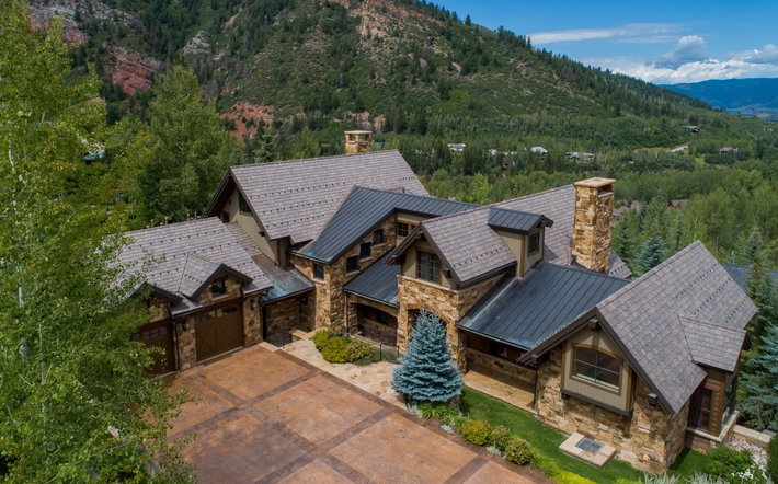 Large stone and wood mountain house with a dark roof, set among pine trees in a forested hillside.