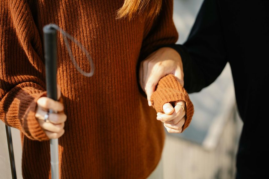 A person is helping a blind woman with a cane.