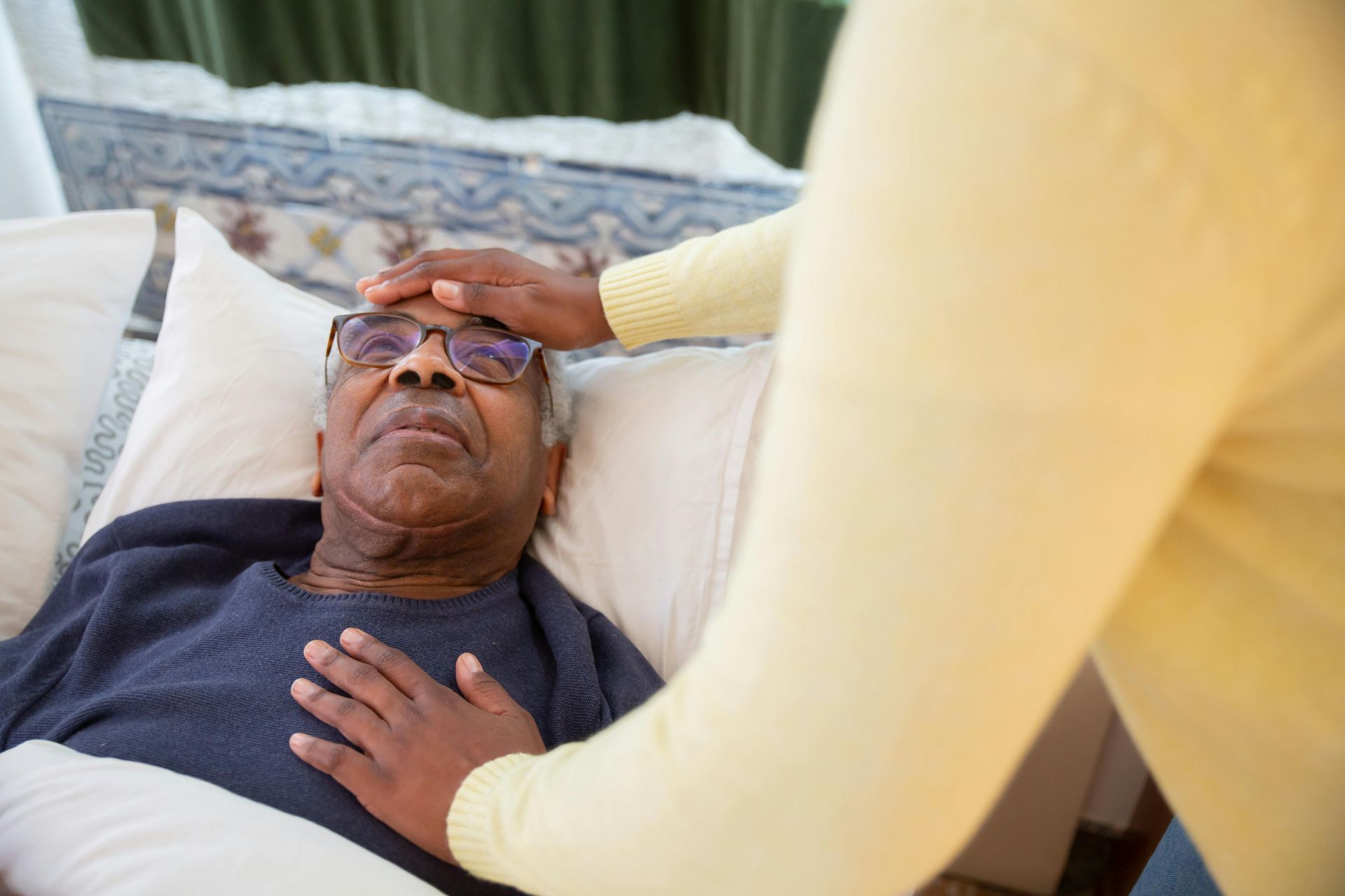 An elderly man is laying in a bed with a nurse touching his forehead.