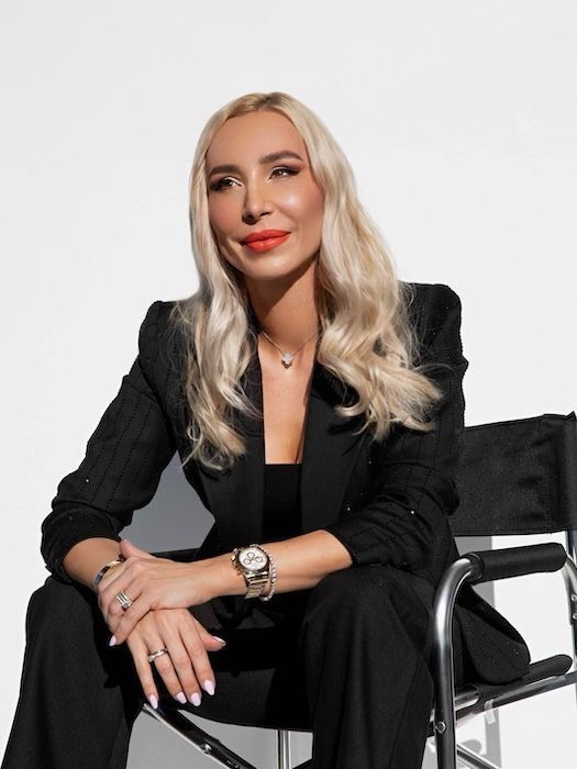 A woman in a black suit is sitting in a director 's chair — Sibina Cosmetic Tattoo Art In Broadbeach, QLD